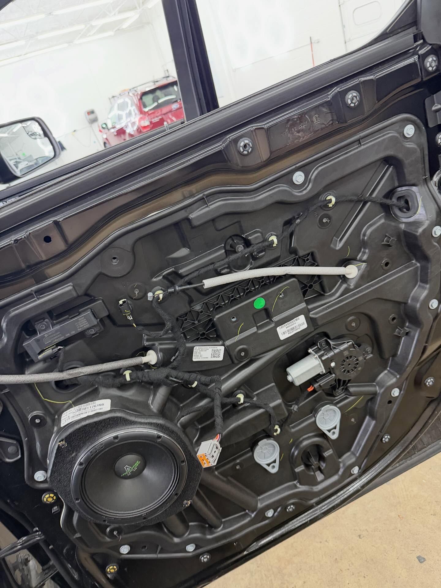 The interior of a car door with the panel removed, showing the speaker, internal wiring, and metal door frame.