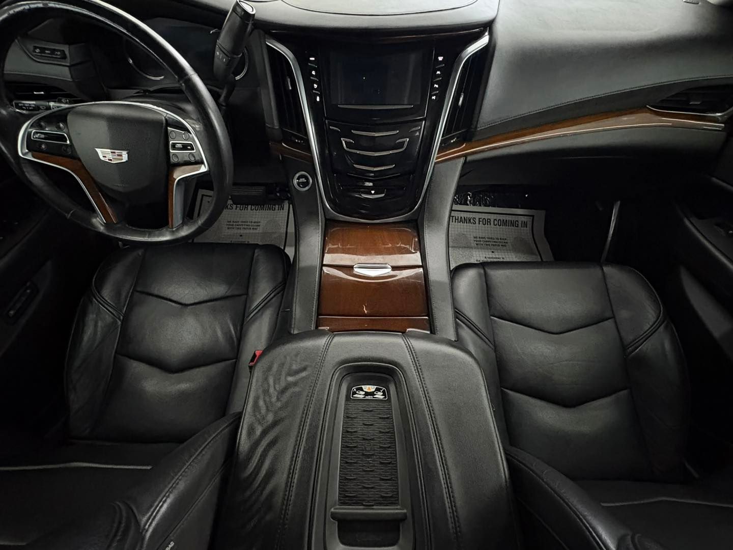 The interior of a Cadillac vehicle showing black leather seats, a wood-trimmed center console, and a steering wheel.