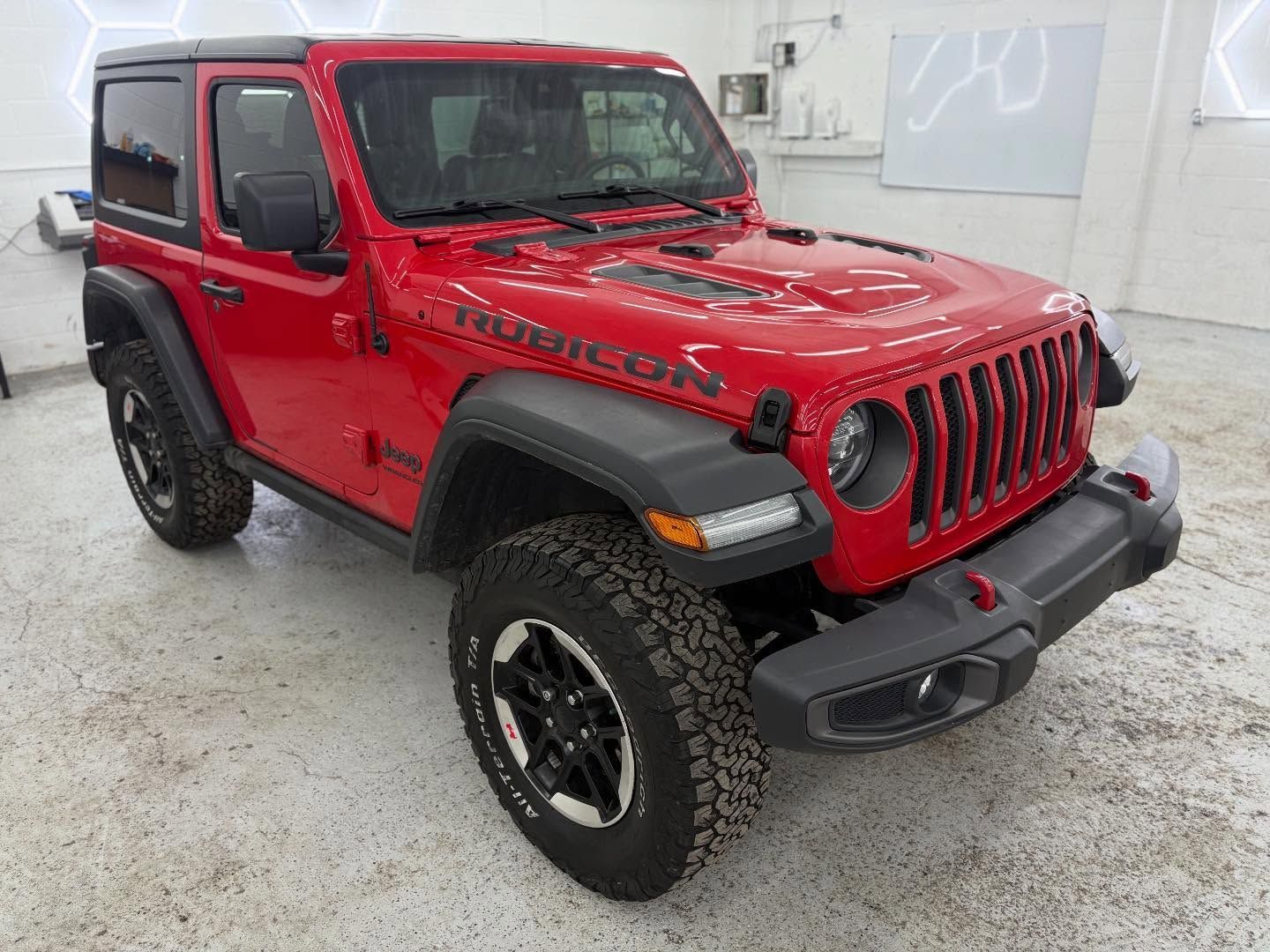 A red Jeep Wrangler Rubicon 2-door SUV parked inside a bright, white-walled garage.