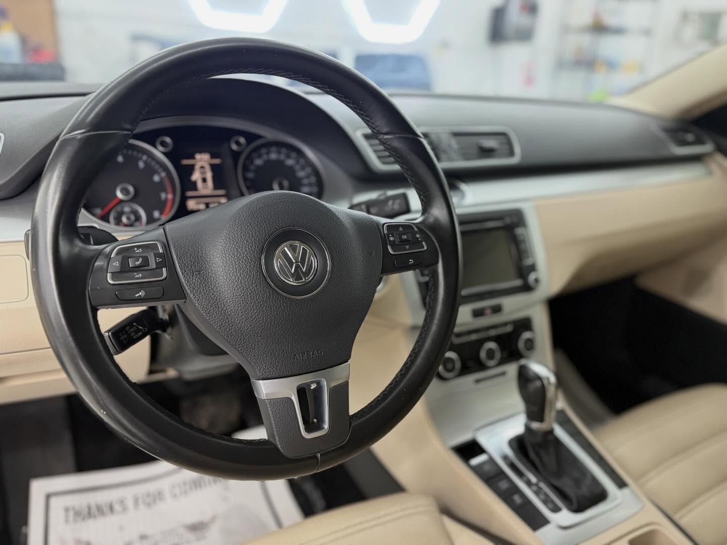Interior of a Volkswagen car showing the steering wheel, dashboard, and gear shifter with tan upholstery.