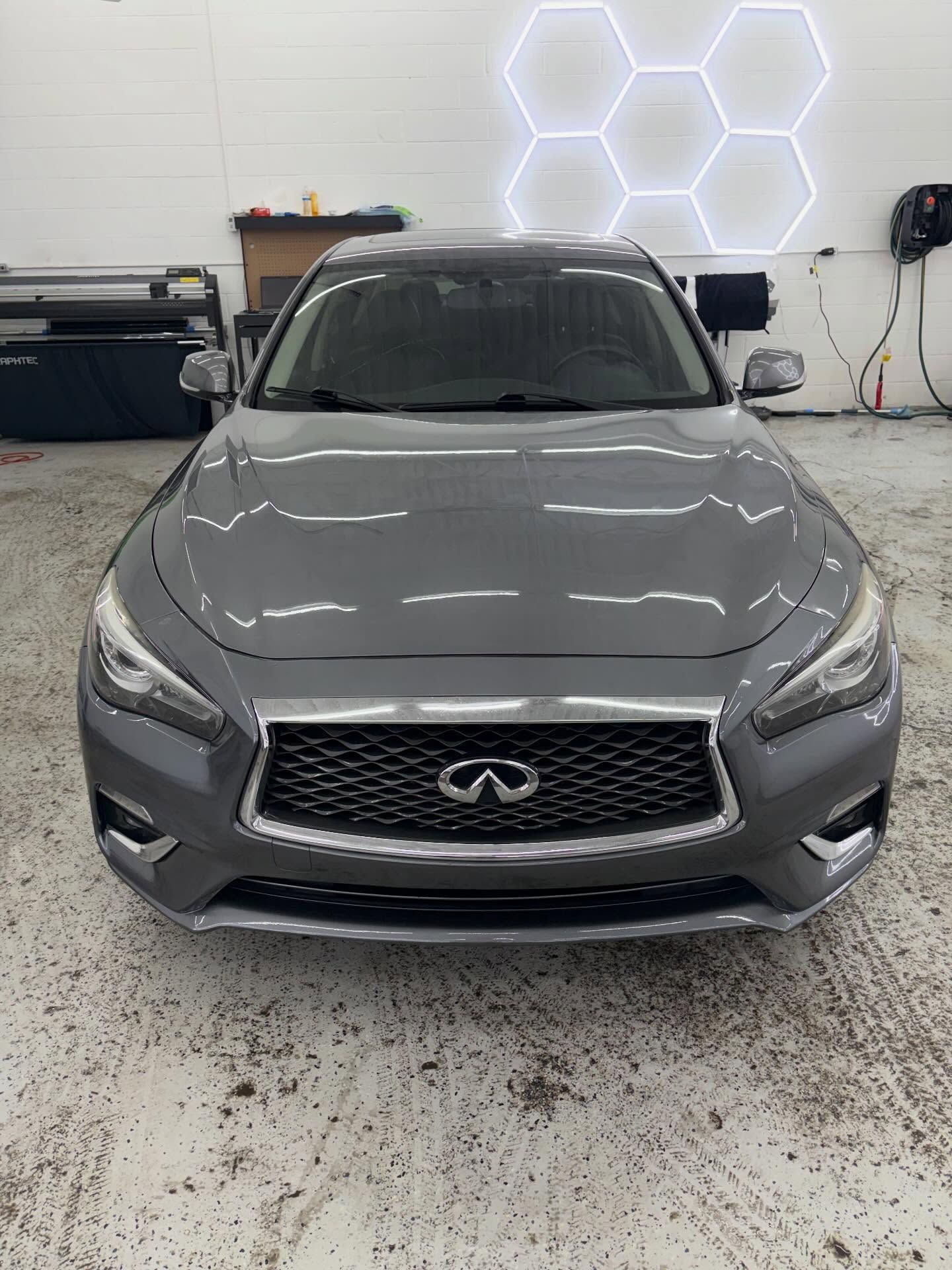 A grey Infiniti sedan parked in a garage with geometric LED wall lighting.