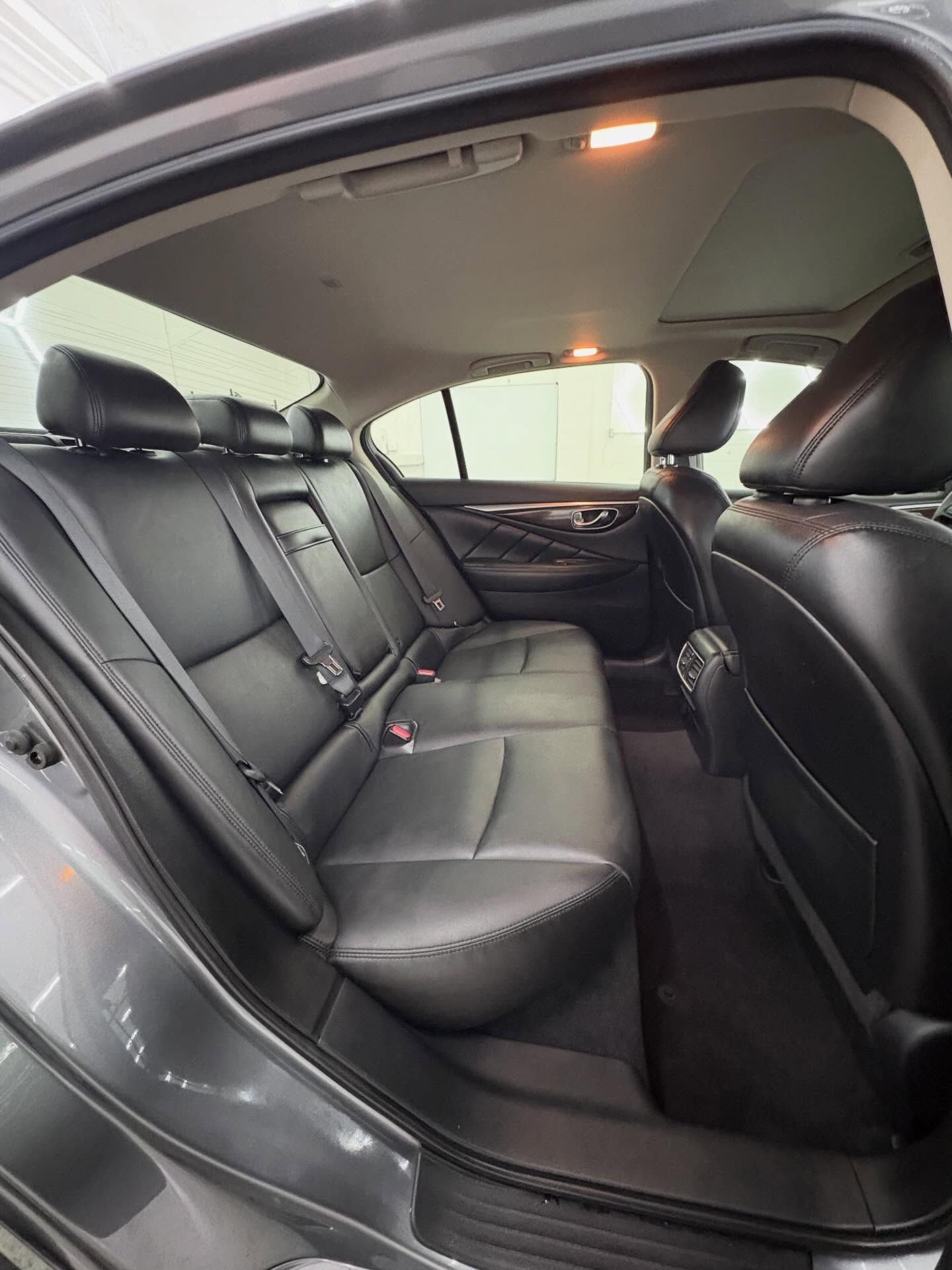 Back seat of a car interior with black leather upholstery, rear headrests, seatbelts, and a partial view of a sunroof.