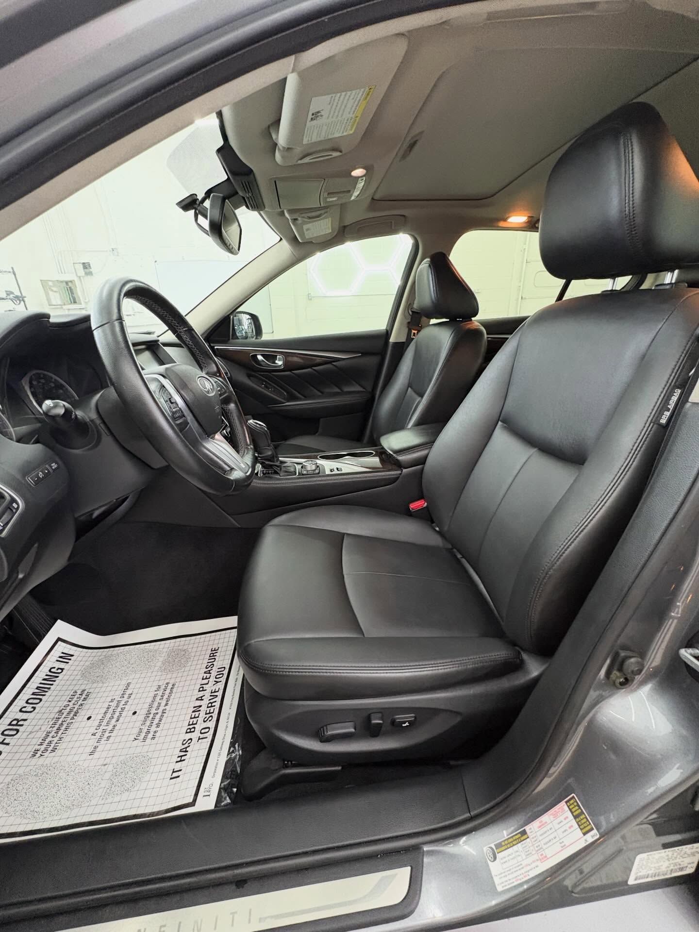 The interior front cabin of a car featuring black leather seats, a steering wheel, and a sunroof.