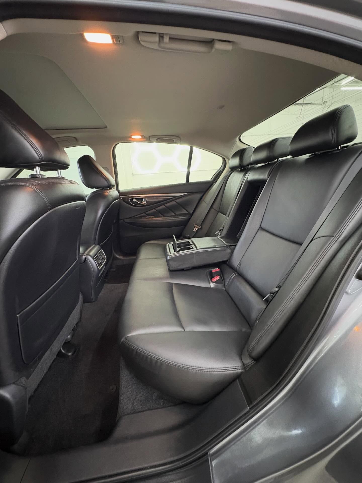 Interior view of a gray car's back seat, featuring black leather upholstery and a fold-down center armrest with cupholders.