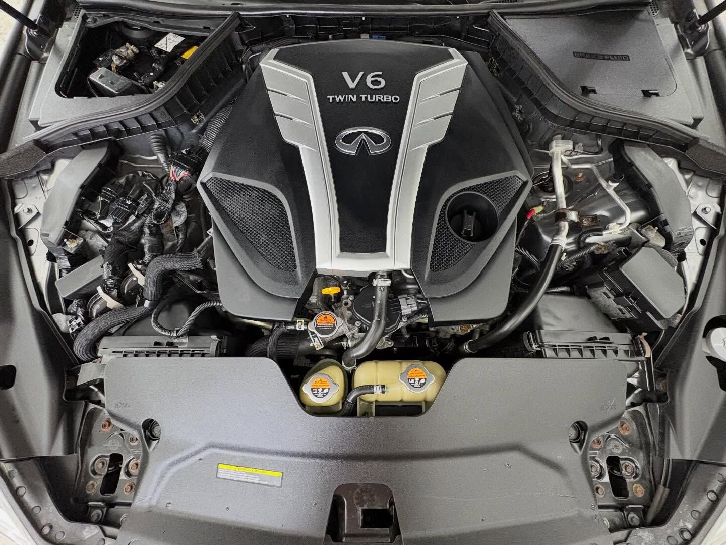 Top-down view of an Infiniti V6 twin-turbo car engine inside an open hood, showing plastic covers and mechanical parts.