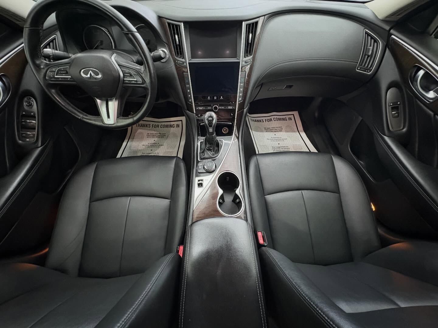 The interior of a black Infiniti car, showing leather seats, a steering wheel, and a center console dashboard from above.