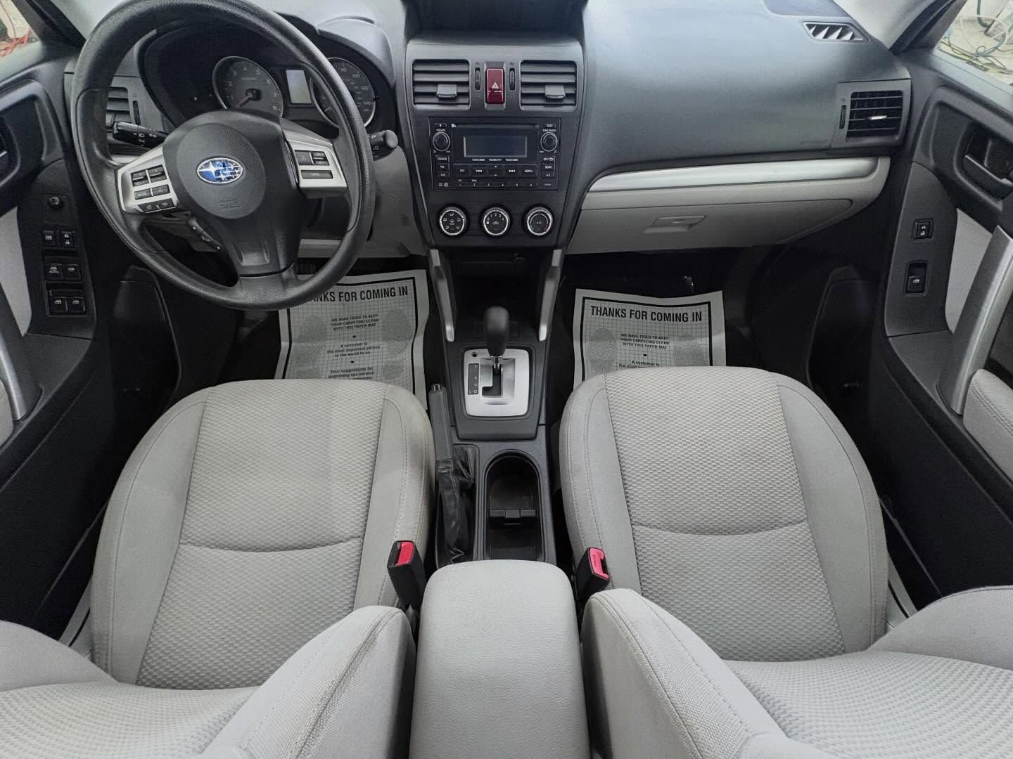 Front view of a Subaru car interior featuring light gray fabric bucket seats, a black dashboard, and a steering wheel.