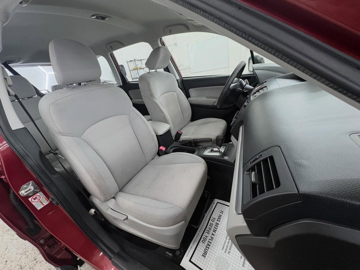 Interior of a maroon car with light gray fabric bucket seats and a black dashboard.