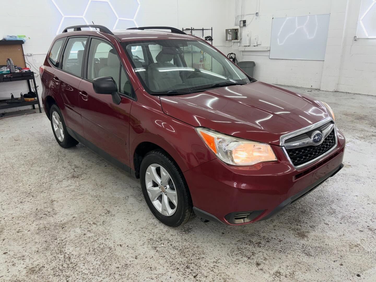 A burgundy Subaru Forester SUV parked inside a brightly lit, industrial-style garage or workshop.