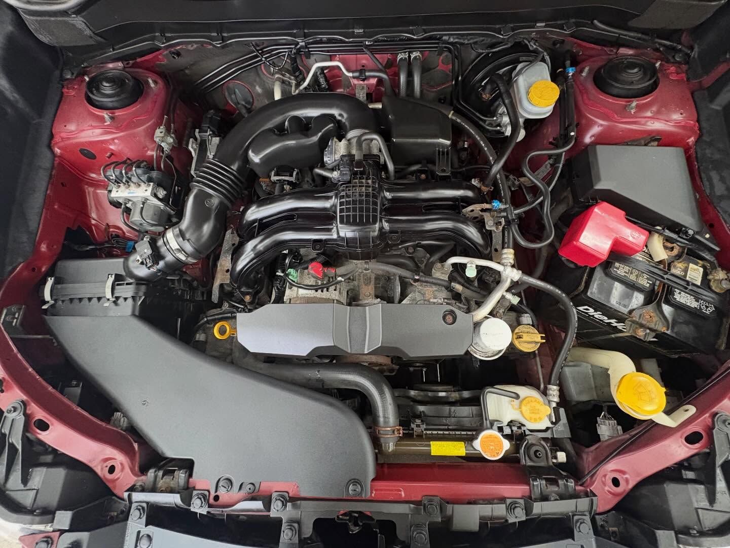 Top-down view of a clean, red-framed car engine bay with various black components, hoses, and bright yellow fluid caps.