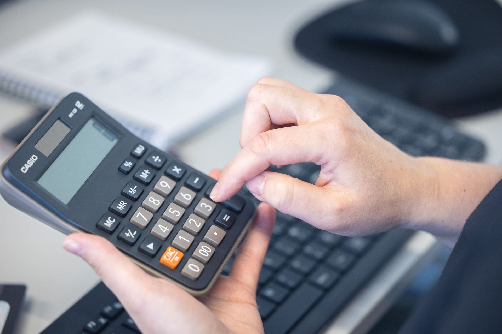 Hands using a calculator at a desk with a keyboard and mouse in the background