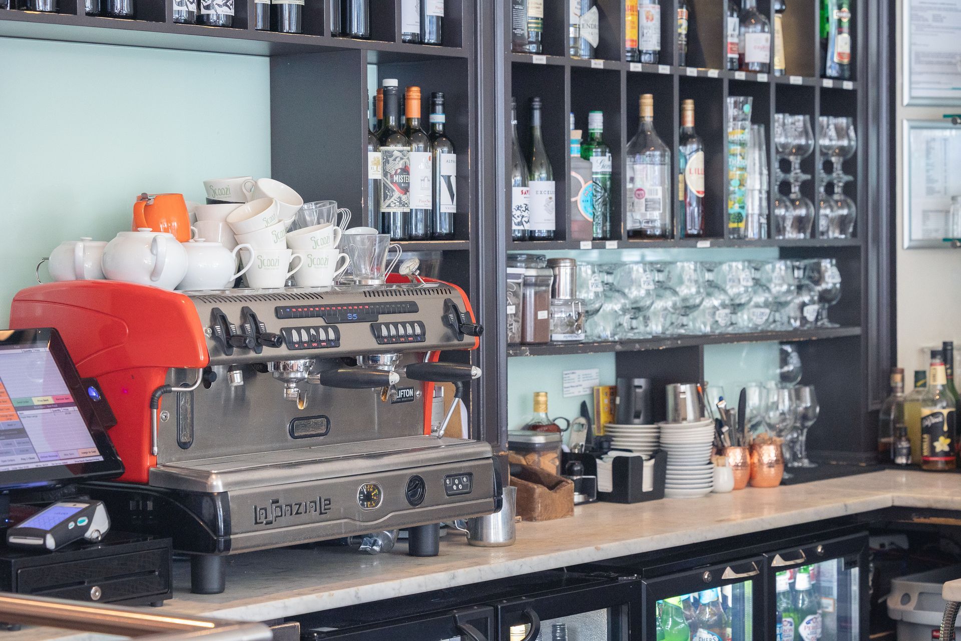 Cafe counter with espresso machine, cups, and shelves of glassware and bottles