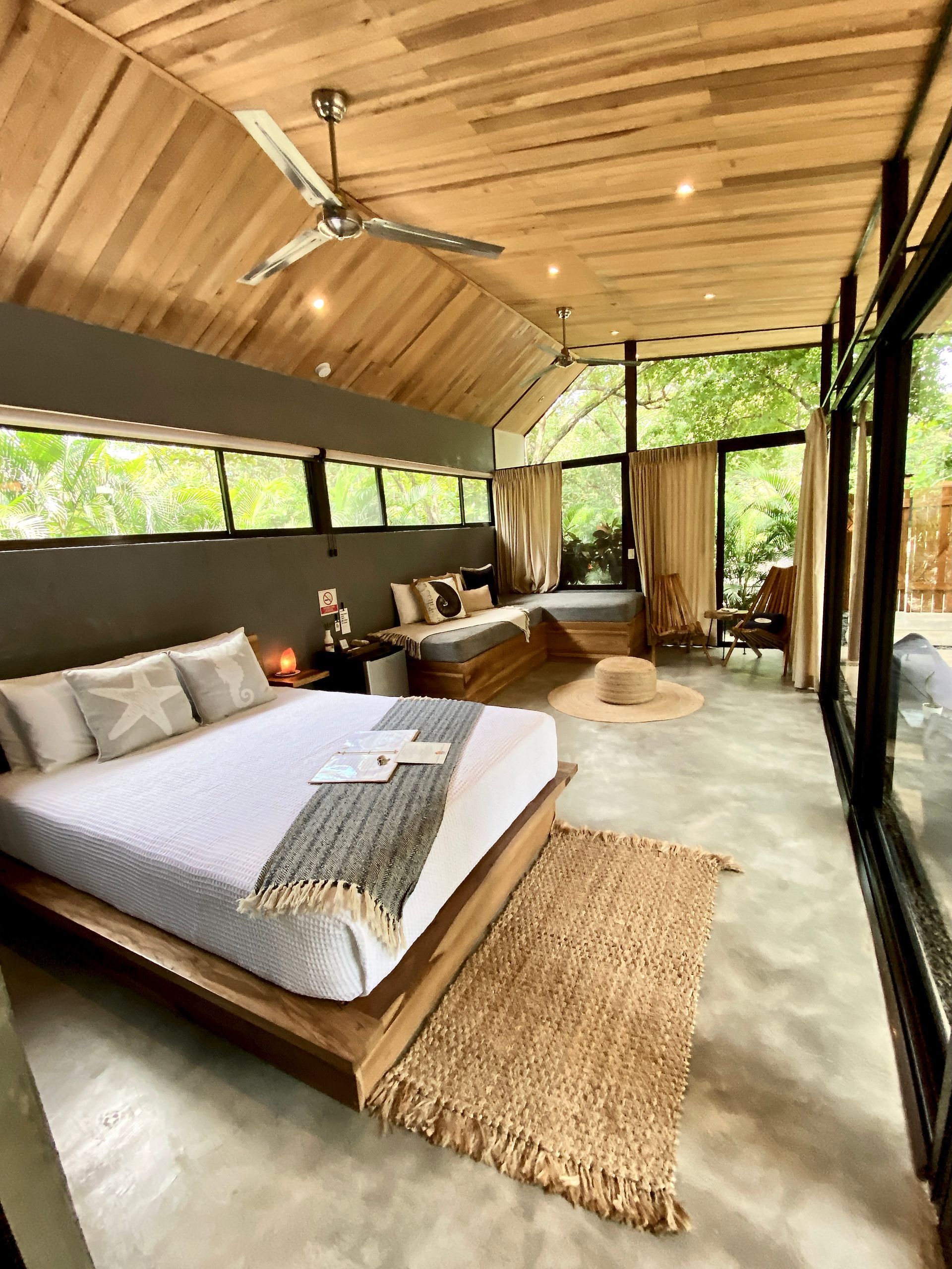 Spacious bedroom with a wooden ceiling, large windows, and a low wooden bed.