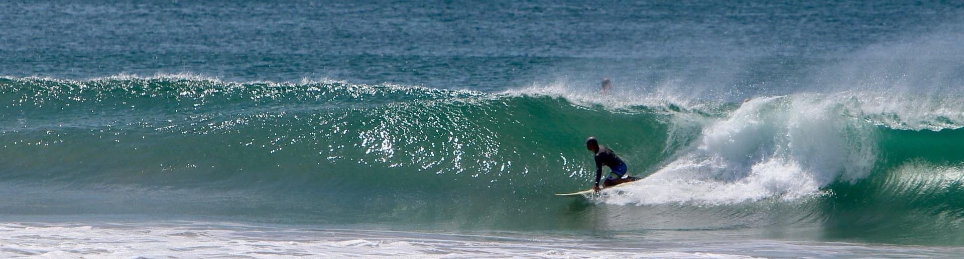 Surfer rides a green wave in the ocean. Blue water, bright sky.
