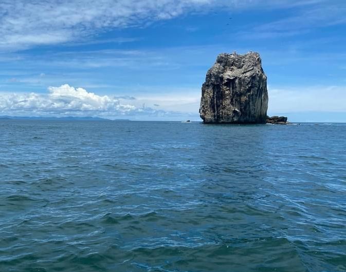 Large rock formation in the ocean under a blue sky with some clouds.
