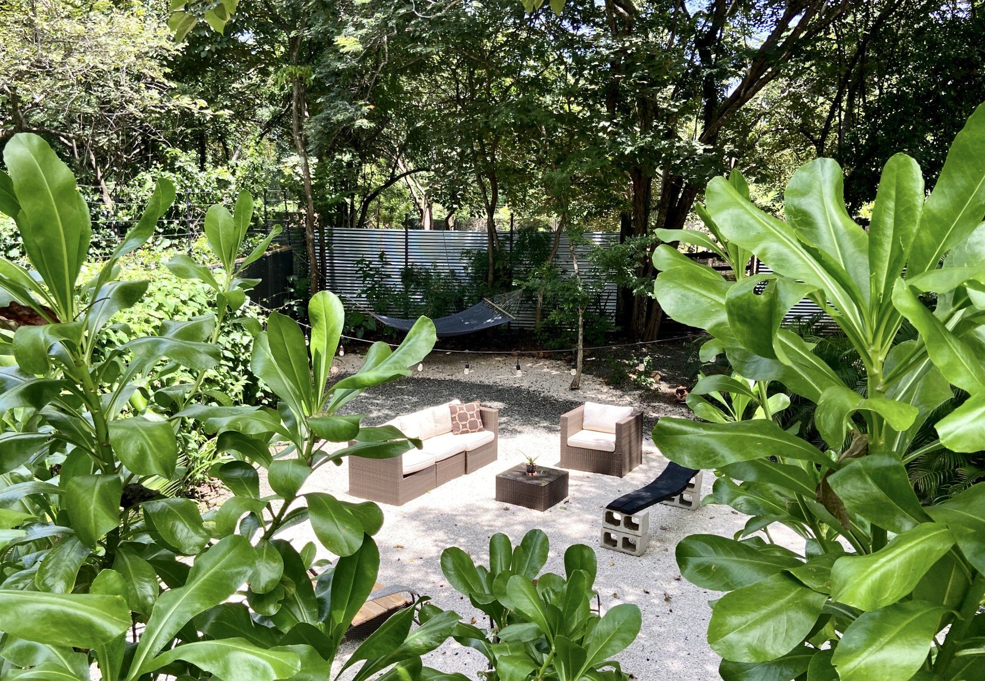 Outdoor seating area surrounded by lush green foliage, white gravel, and a fence.