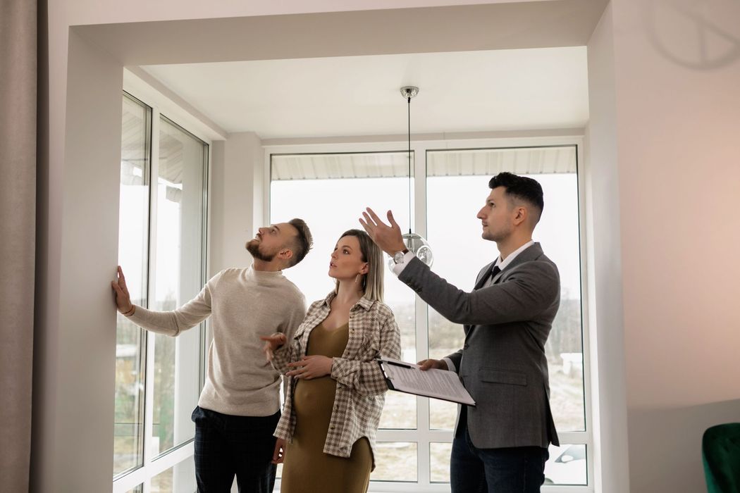 Four people standing in a bright loft kitchen, looking at the room and one holding papers