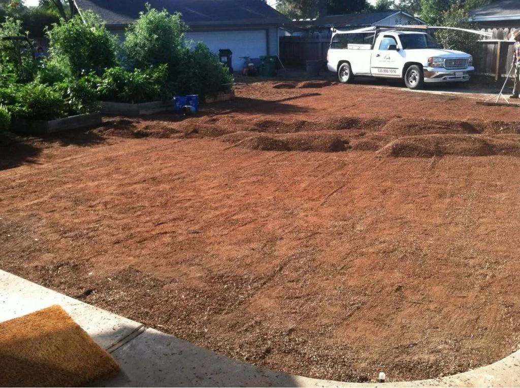 A brown, raked dirt yard showing preparation for new landscaping, with a white truck parked in the background.