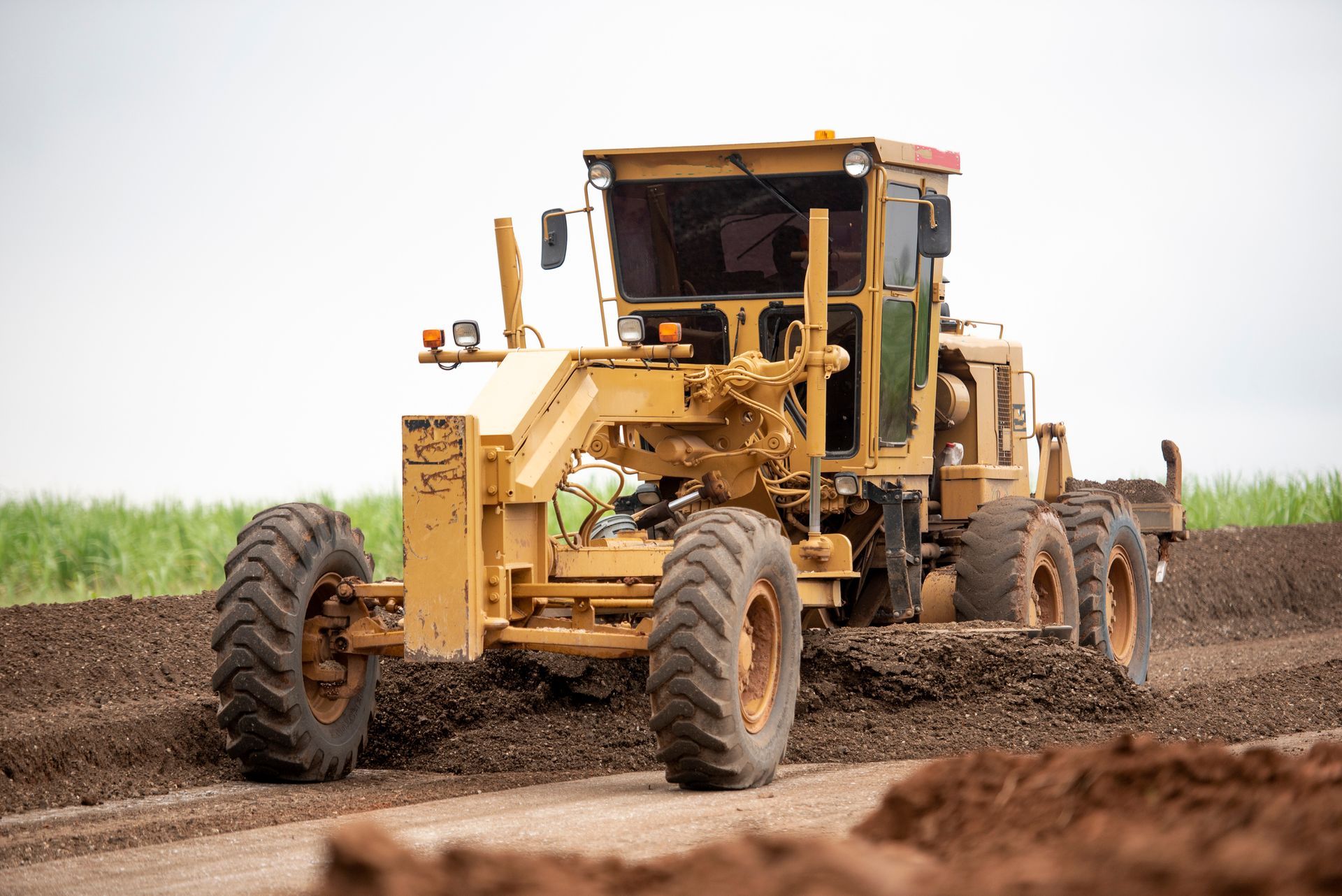 Yellow road grader smoothing a dirt road in a field.