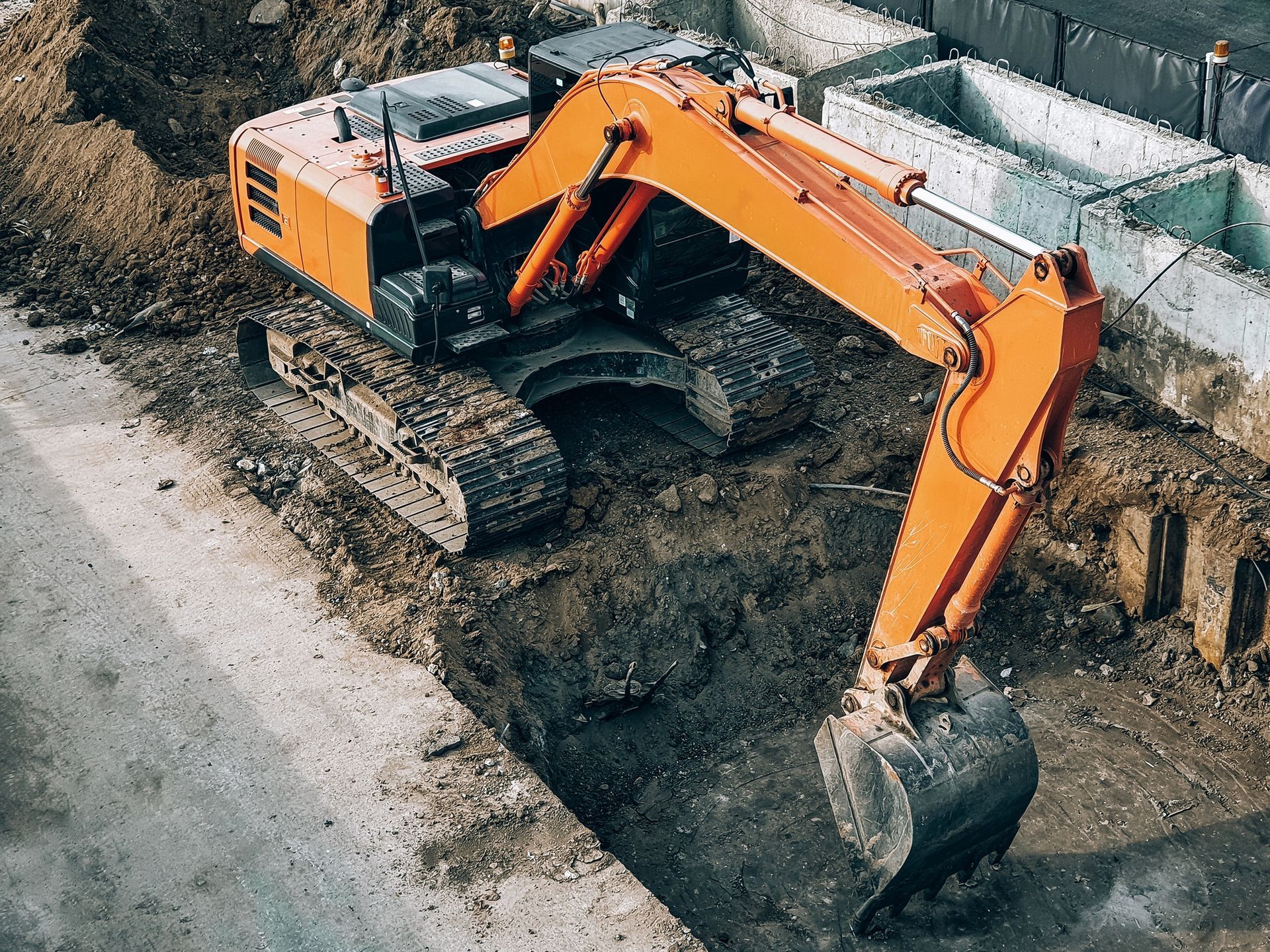 Orange excavator digging a trench near a concrete structure.