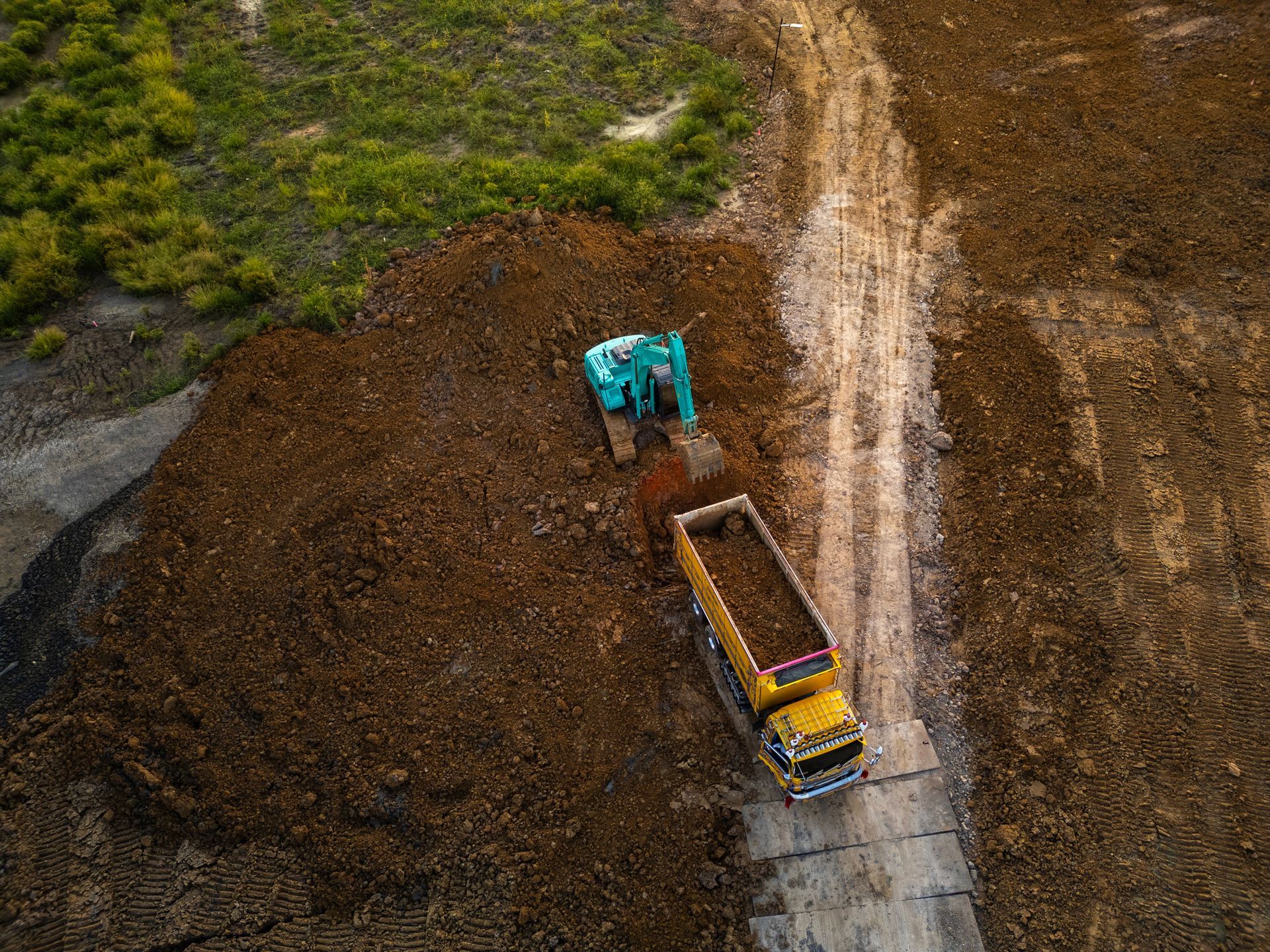 Excavator loading dirt into a yellow dump truck on a construction site.