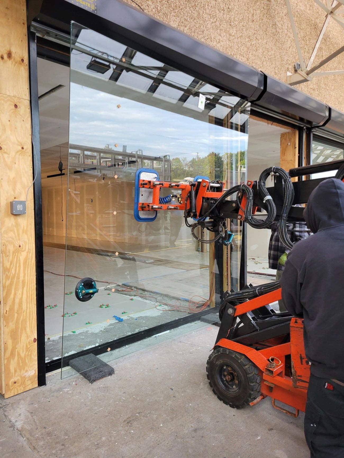 A man is standing next to a machine that is lifting a large glass window.
