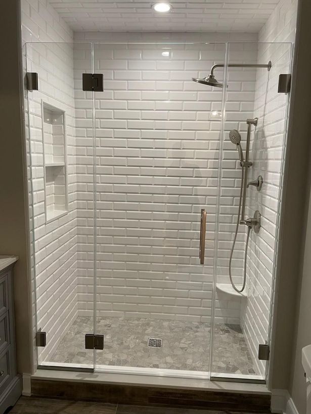 A bathroom with white brick walls and a walk in shower with a glass door.