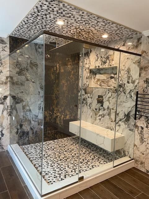 A bathroom with marble walls and a walk in shower with sliding glass doors.