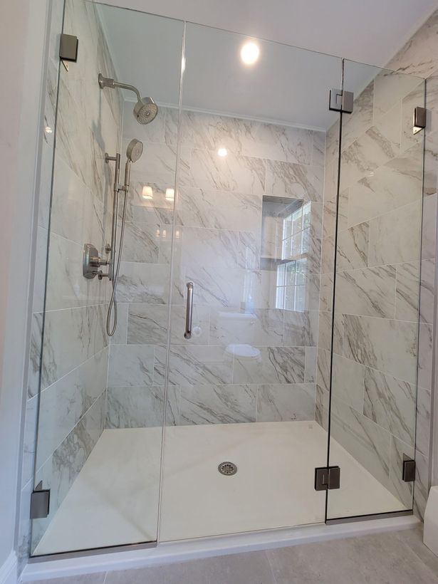 A bathroom with a walk in shower with a glass door and marble walls.