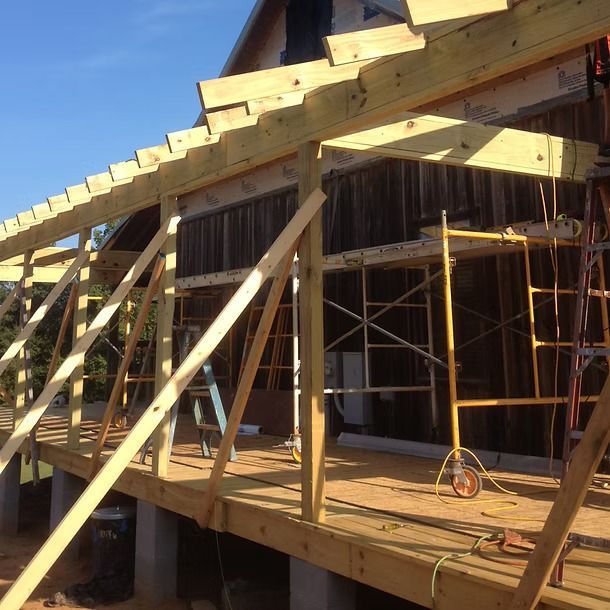 Wood-framed house under construction with scaffolding and angled support beams on a sunny day