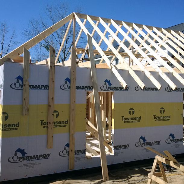 Partially framed house under construction with exposed wooden roof trusses and wrapped walls