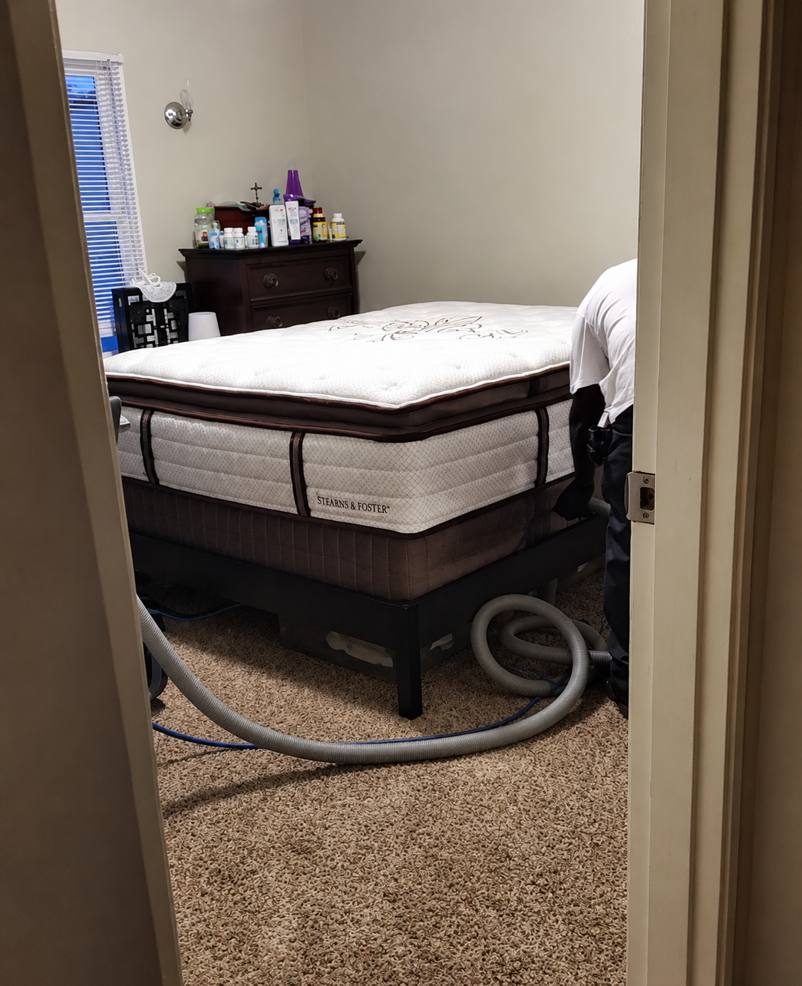 Bedroom with a made bed, dresser, and vacuum hose on carpeted floor.