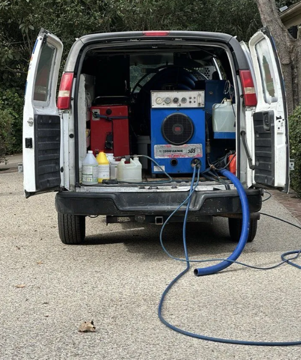Van with open rear doors showing portable carpet-cleaning equipment and hoses at a driveway