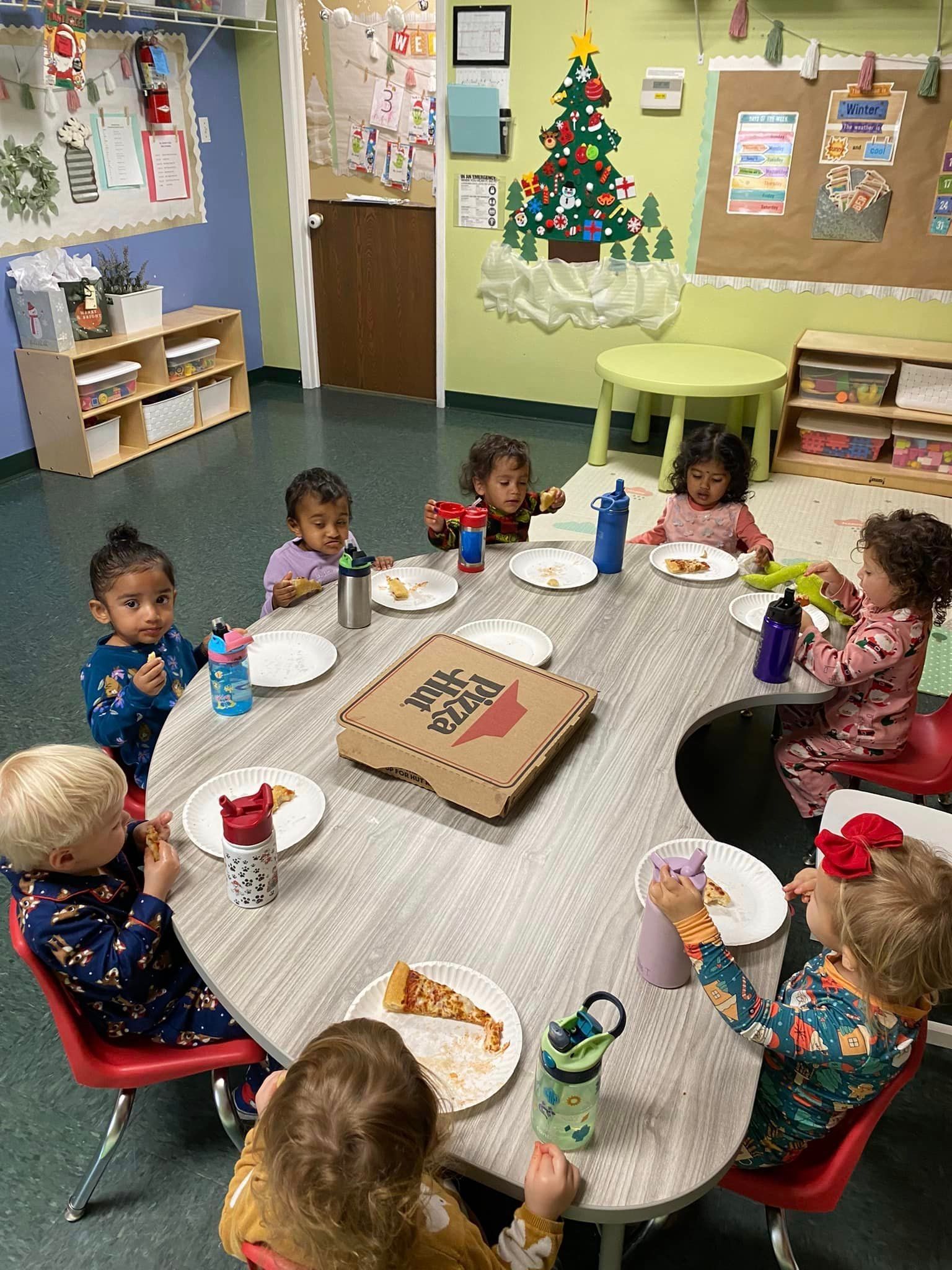 a group of children are sitting around a table eating pizza .