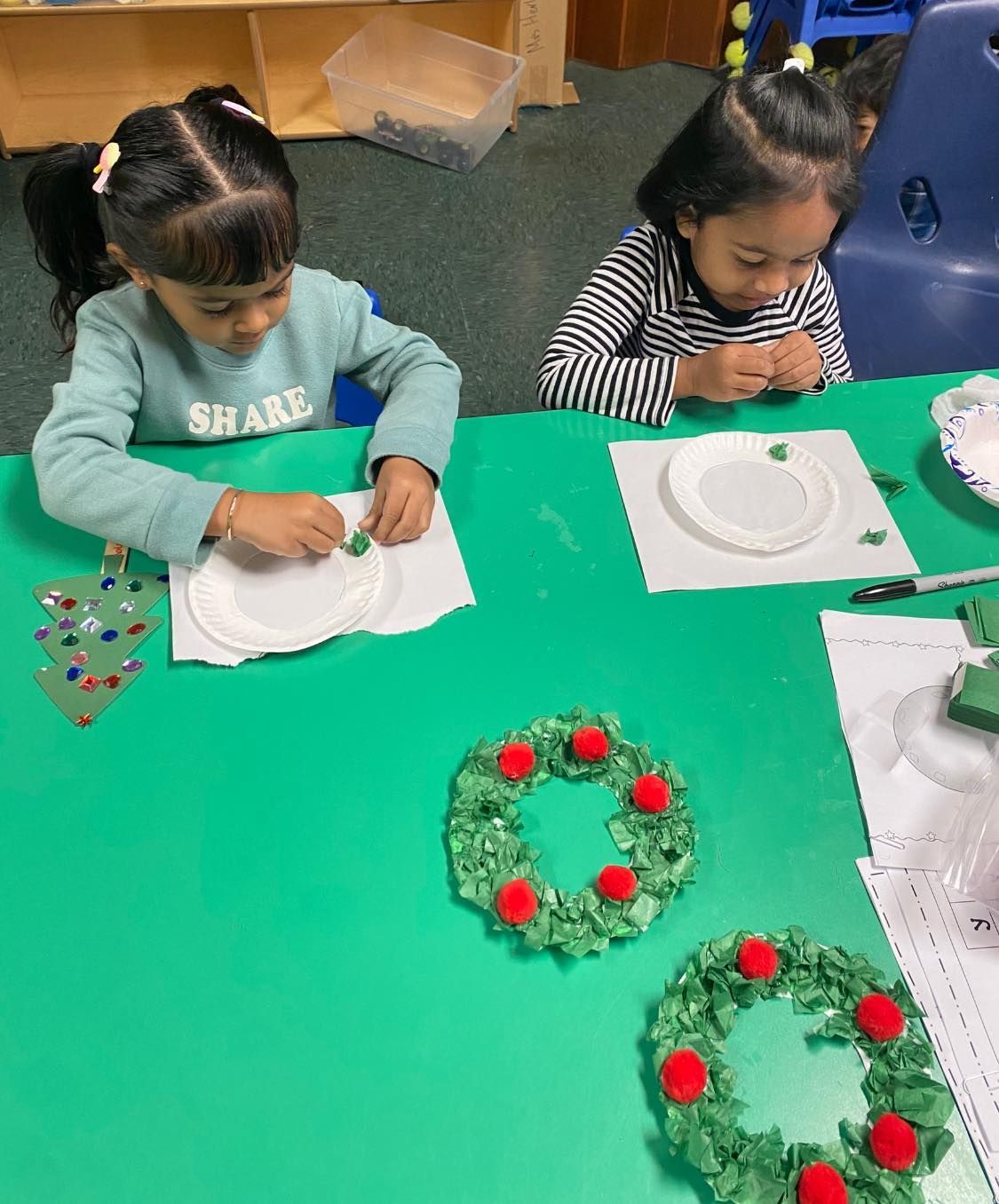 two little girls are sitting at a table making christmas wreaths