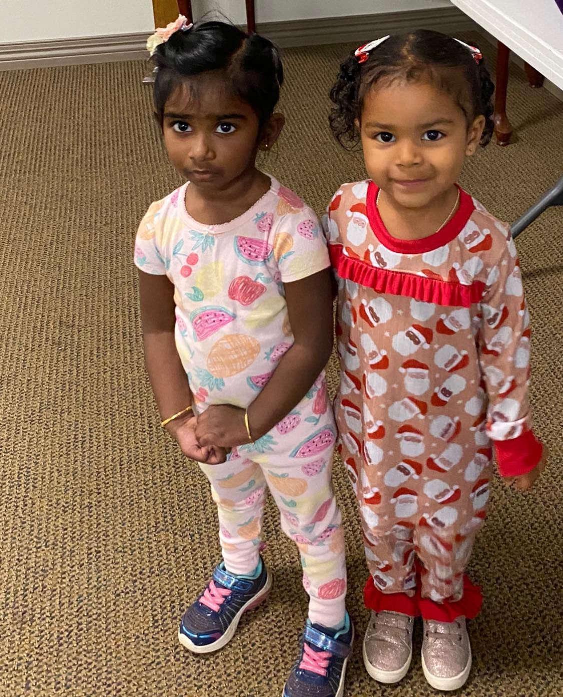 Two little girls are standing next to each other wearing pajamas .