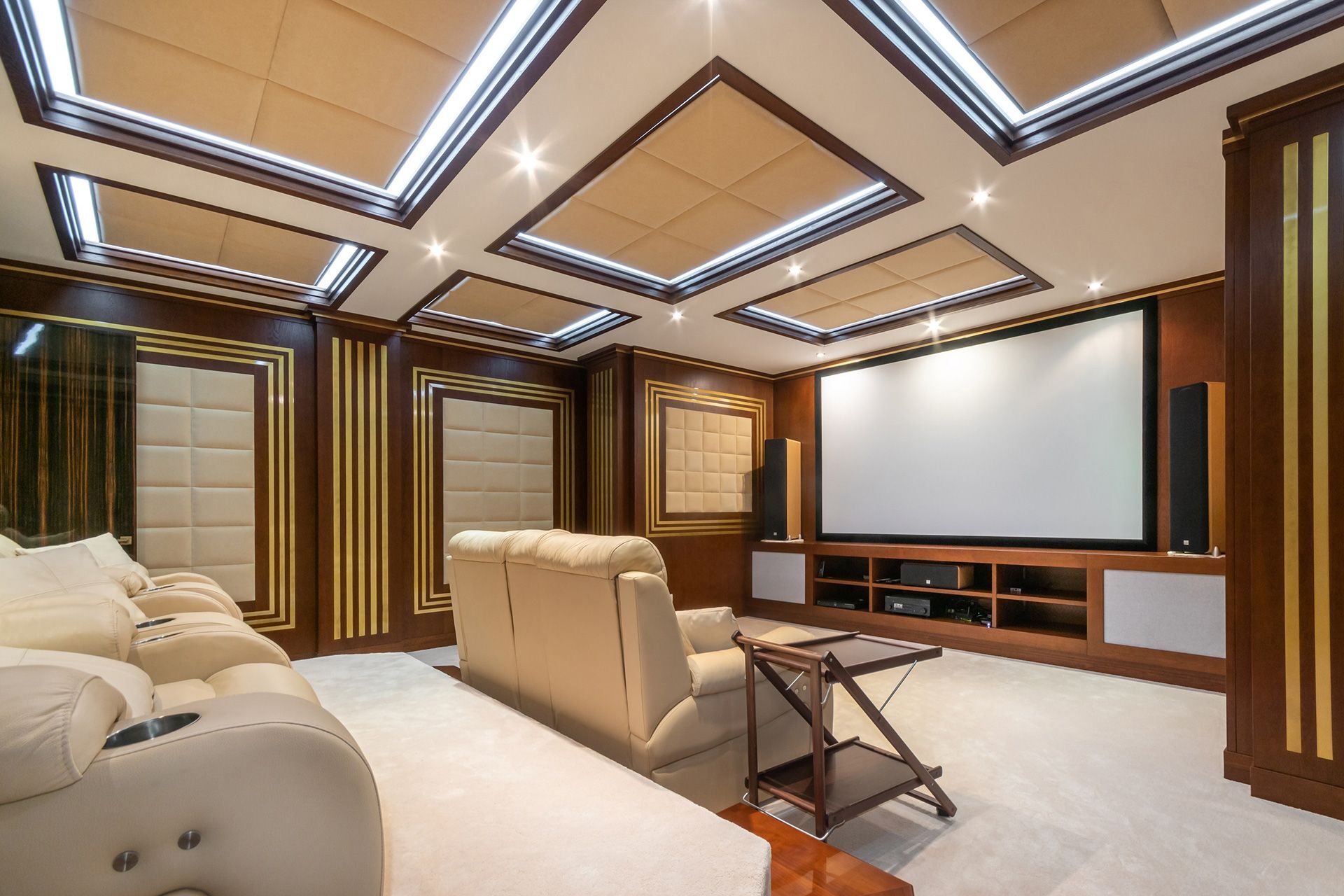 Home theater with cream-colored seating, projector screen, wooden paneling, and a light-colored carpet.