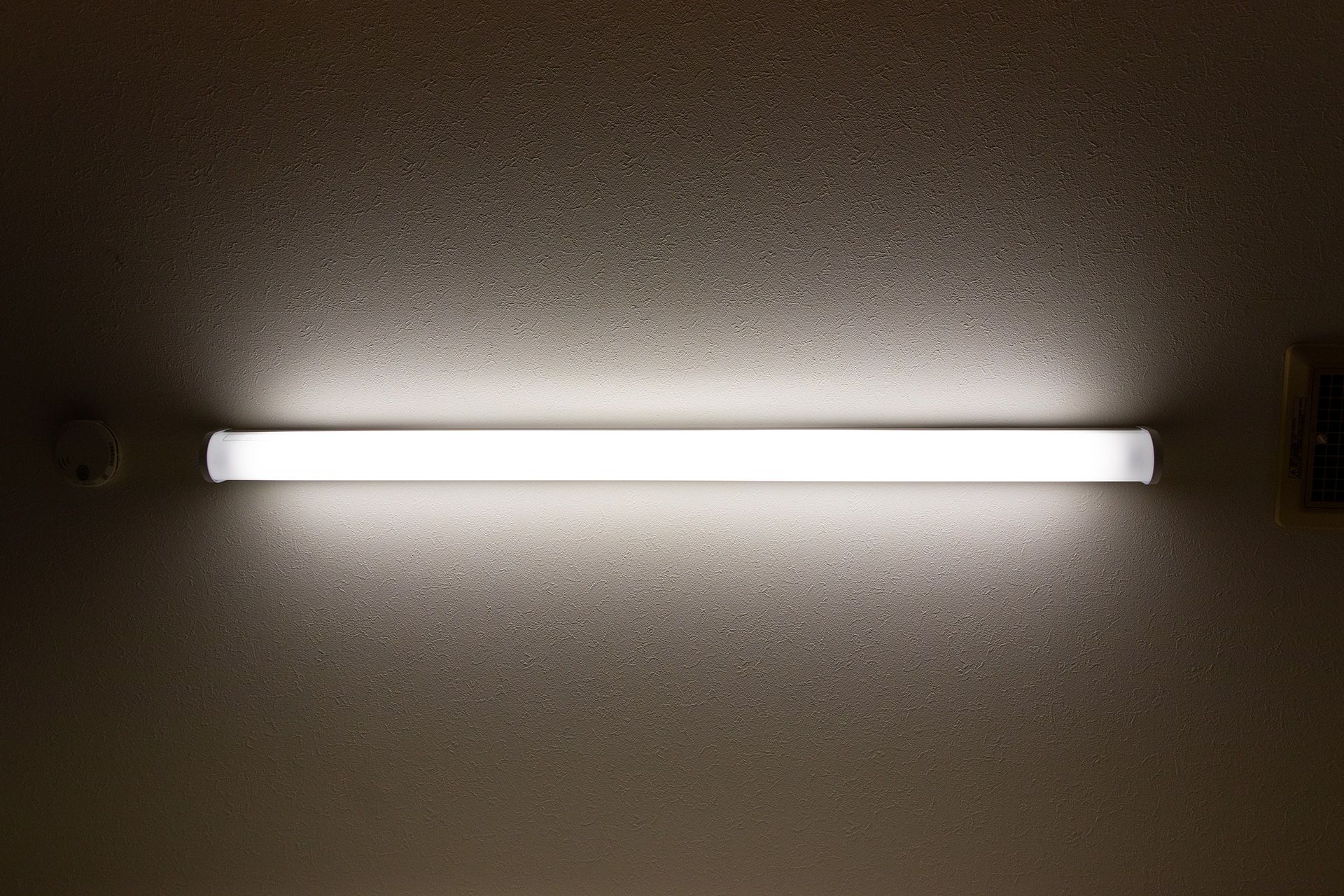 A long, rectangular, fluorescent light fixture illuminates a textured ceiling.
