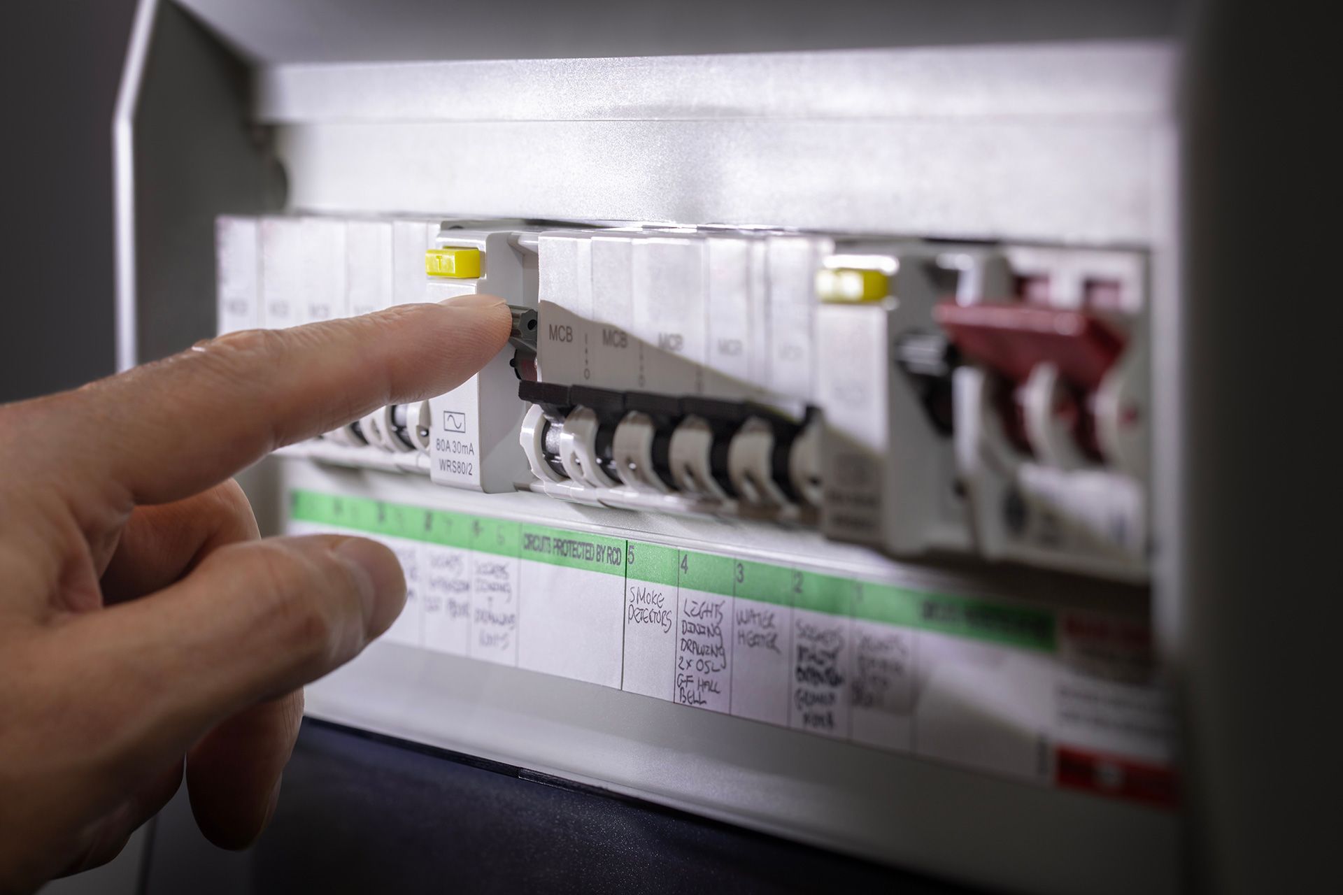 Hand pointing to a tripped circuit breaker in a fuse box.
