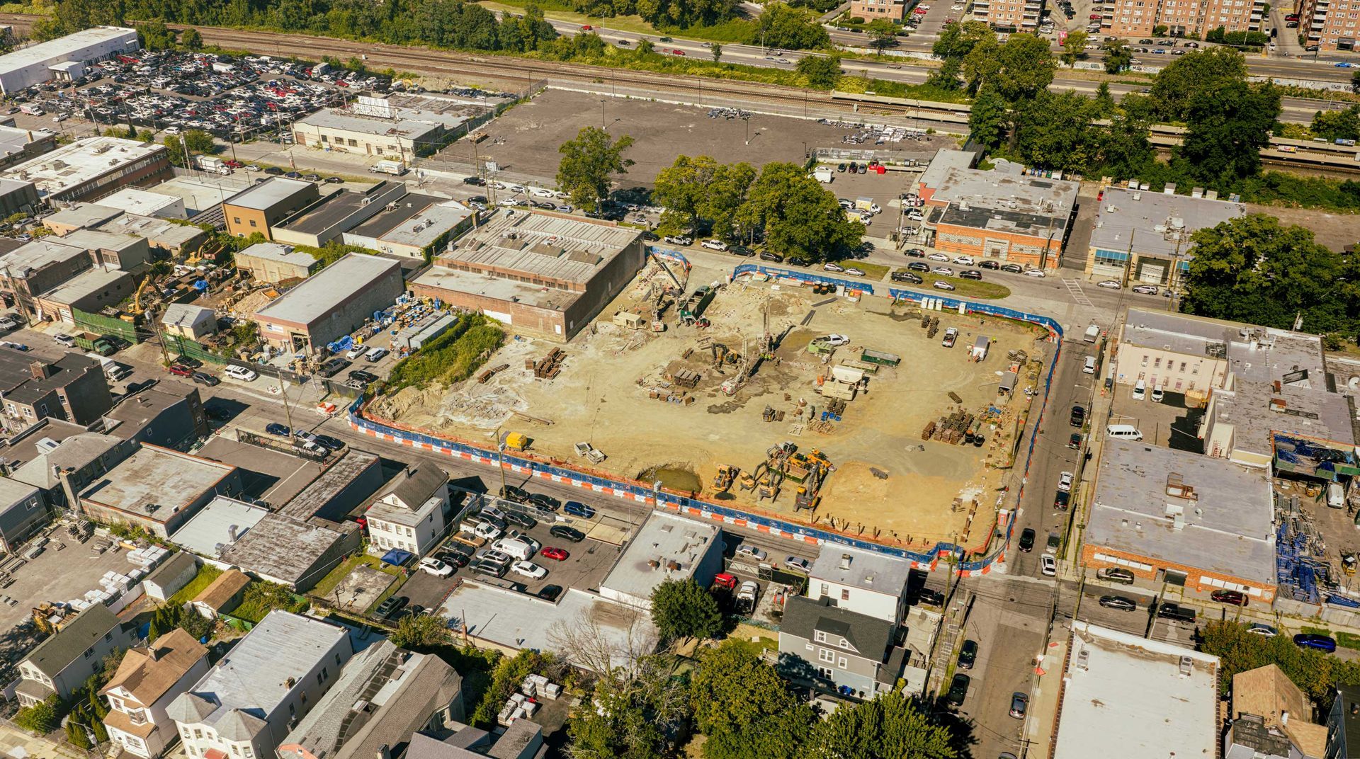 Aerial view of a cleared construction site surrounded by buildings in a city neighborhood.