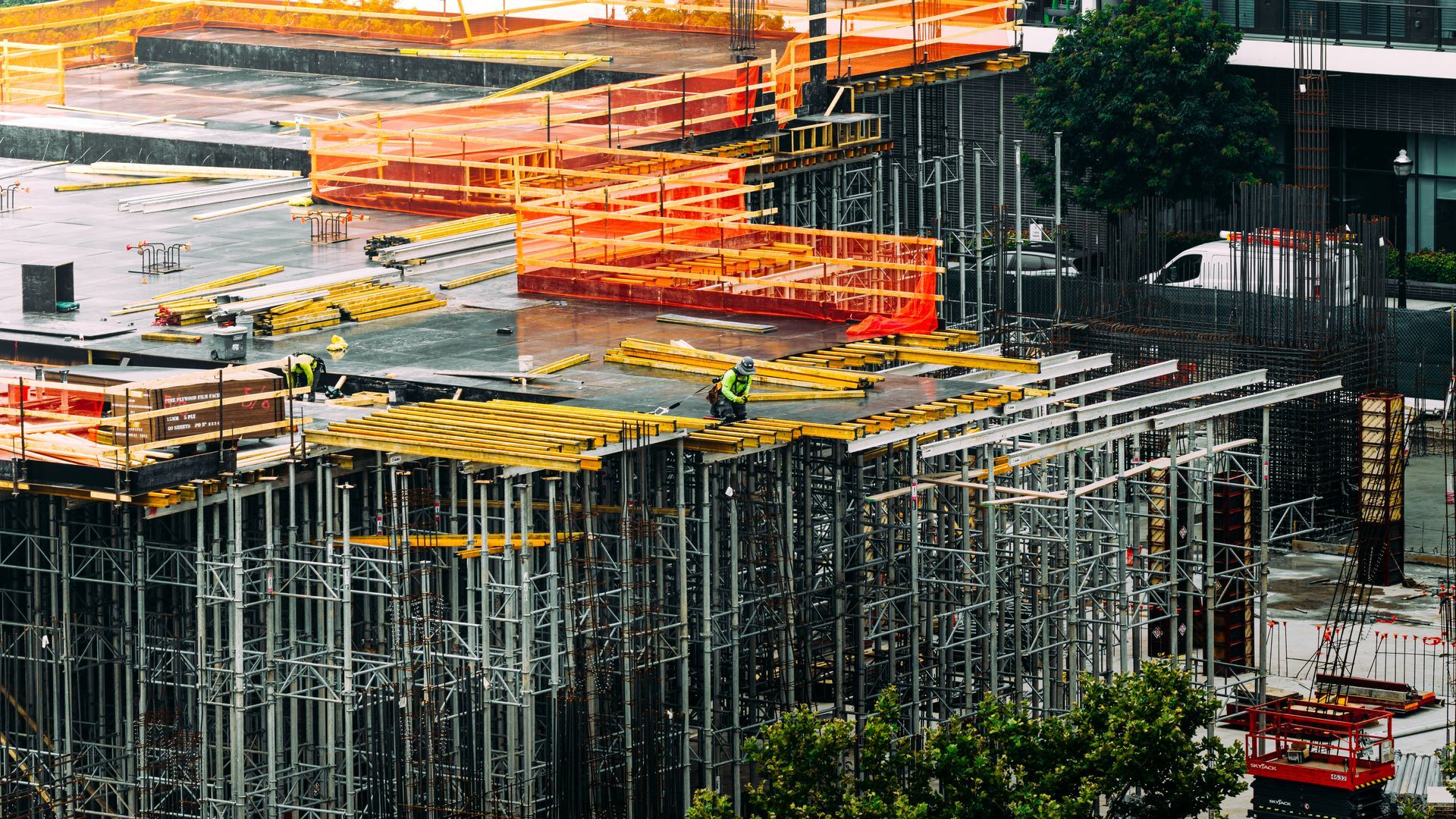 Construction site with scaffolding and orange safety barriers, several workers.