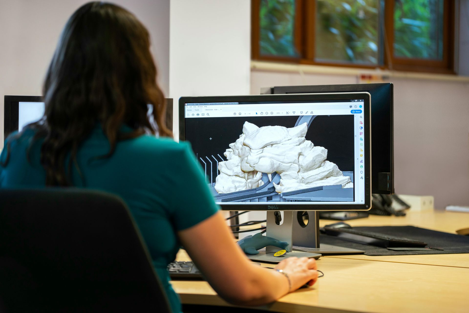 Woman at a computer, working on a 3D design of a building.