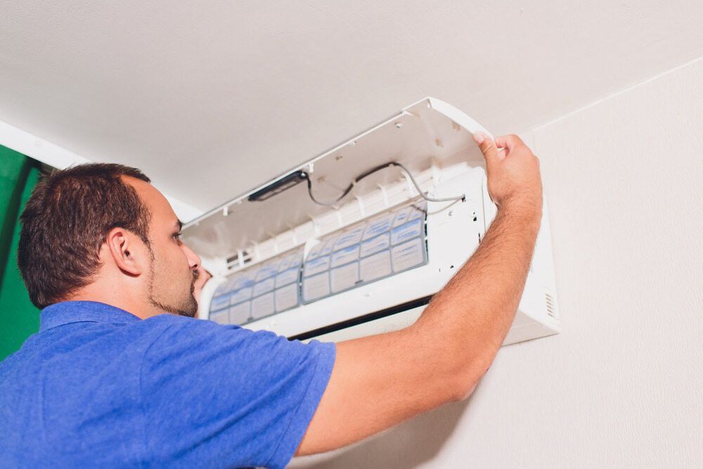 A Man Is Fixing An Air Conditioner On The Wall — Bear Air Conditioning In Gosford, NSW
