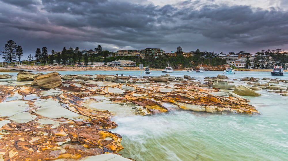 A Beach With Rocks And Boats In The Water On A Cloudy Day — Bear Air Conditioning In Gosford, NSW