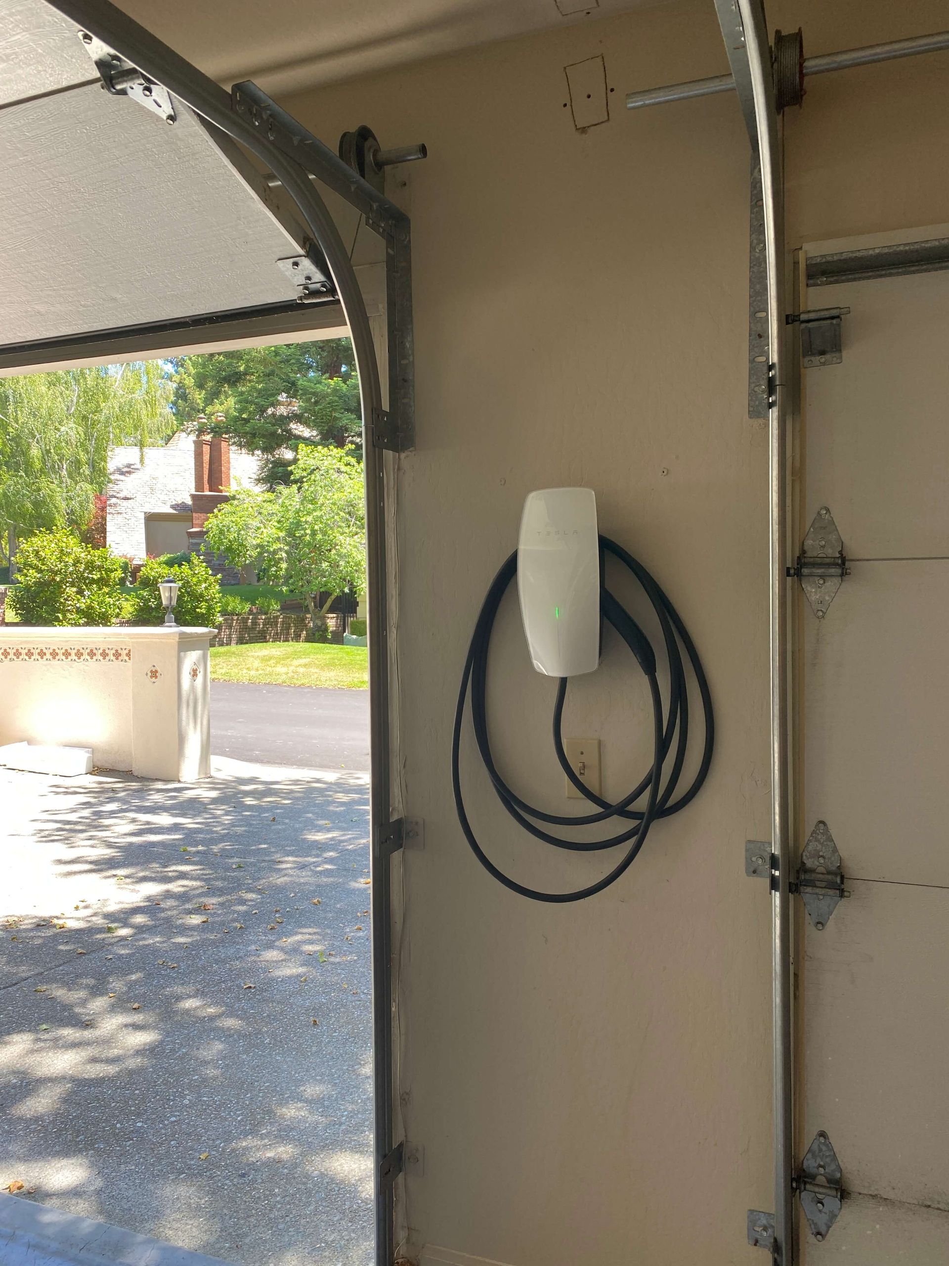 Garage wall with an electric vehicle charger and coiled charging cable. Garage door is open.
