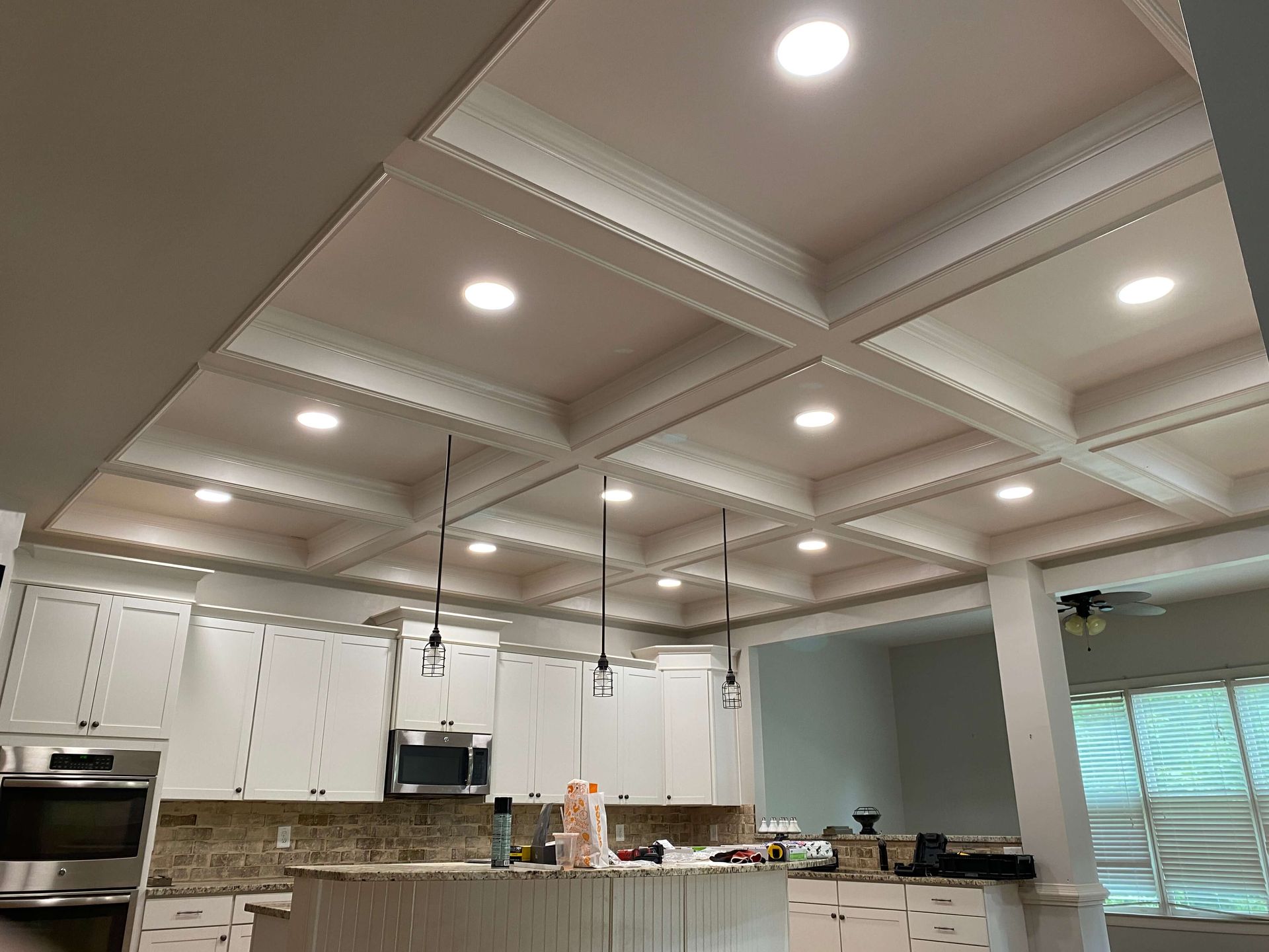 White kitchen with coffered ceiling, recessed lights, and pendant lights over the island.