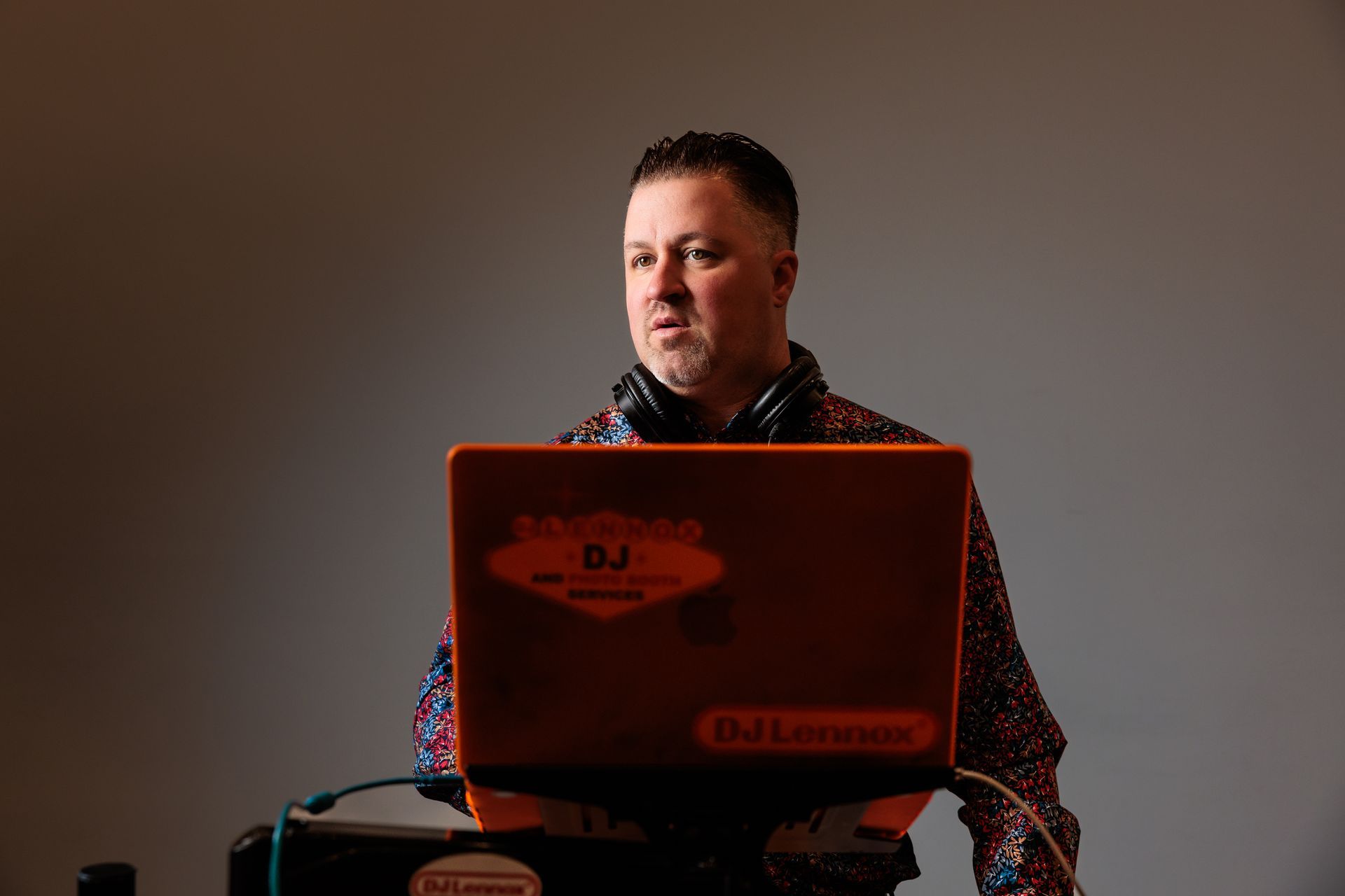 DJ at work, wearing headphones, using a laptop with stickers, in a studio setting.
