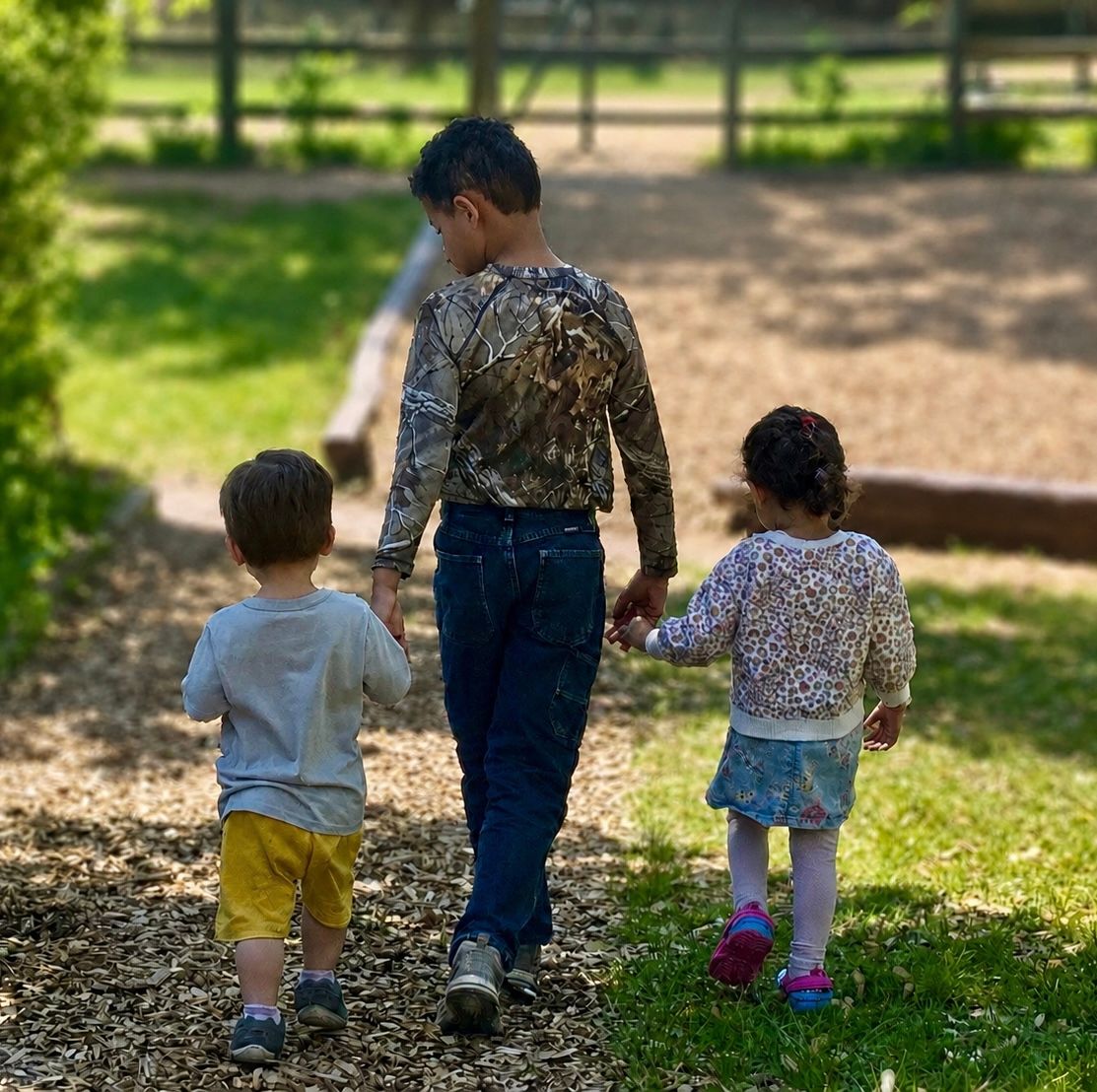 Three children walking hand in hand on a sunny path outdoors