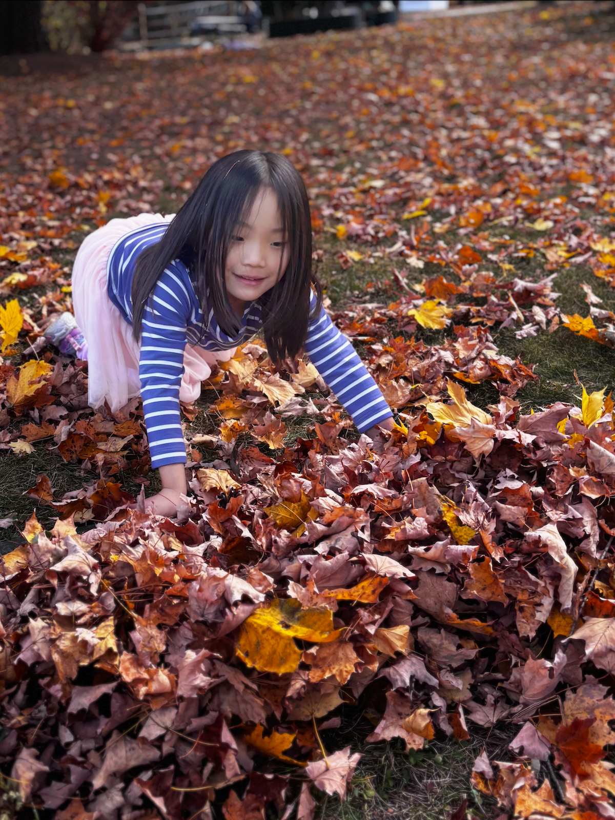 Child in a striped shirt crawling through a pile of autumn leaves outdoors