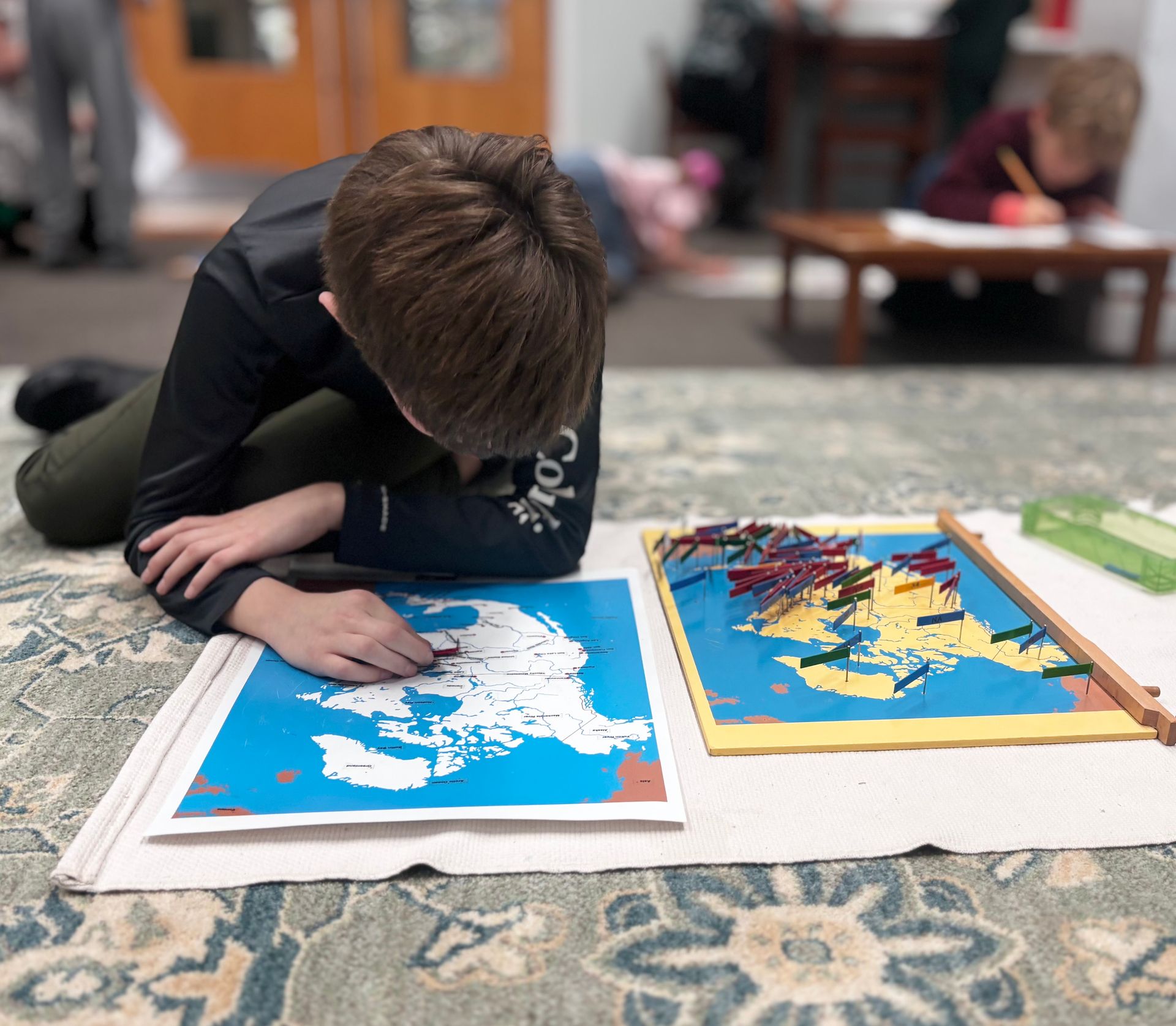 Child tracing a blue-and-white map on the floor beside colorful puzzle boards
